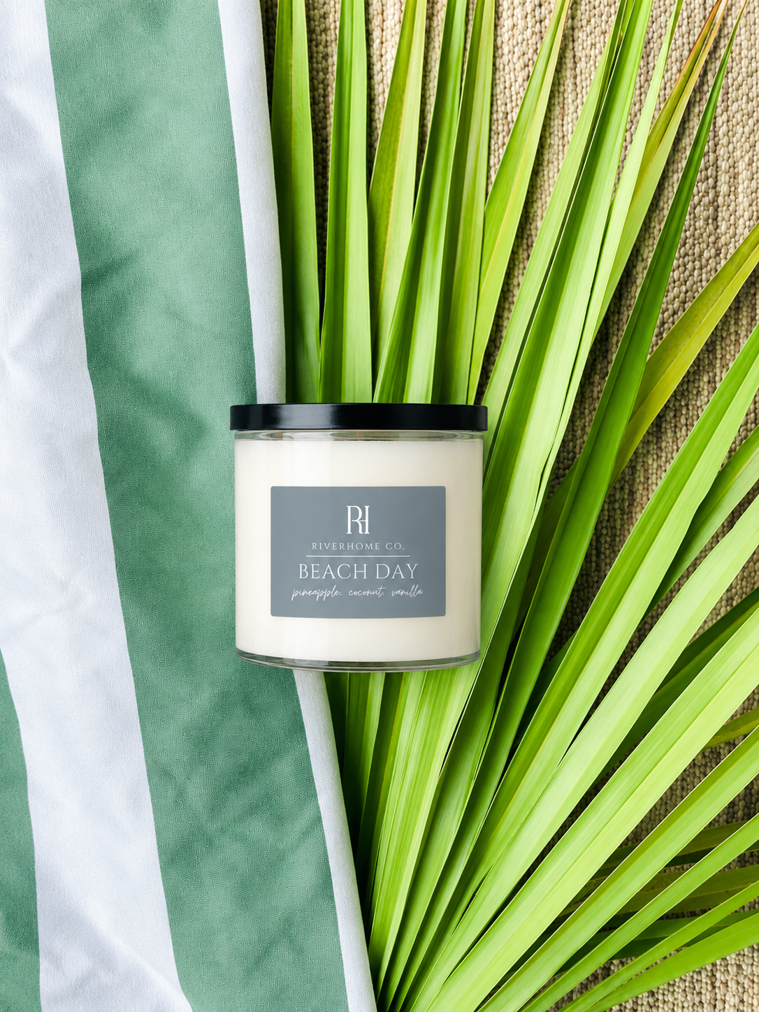 Candle labeled 'Beach Day' by Riverhomeco on a leafy background